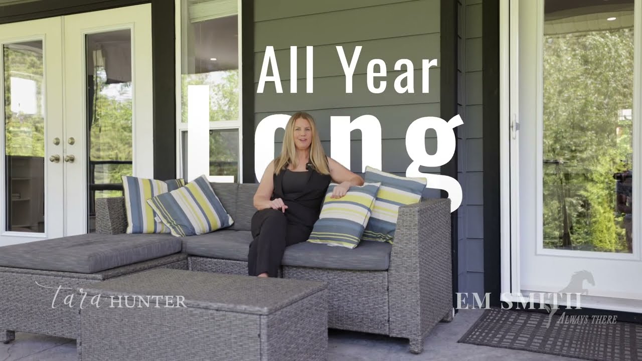 Em Smith sits on an outdoor couch on the covered outdoor entertaining space of a home for sale in Squamish, BC.